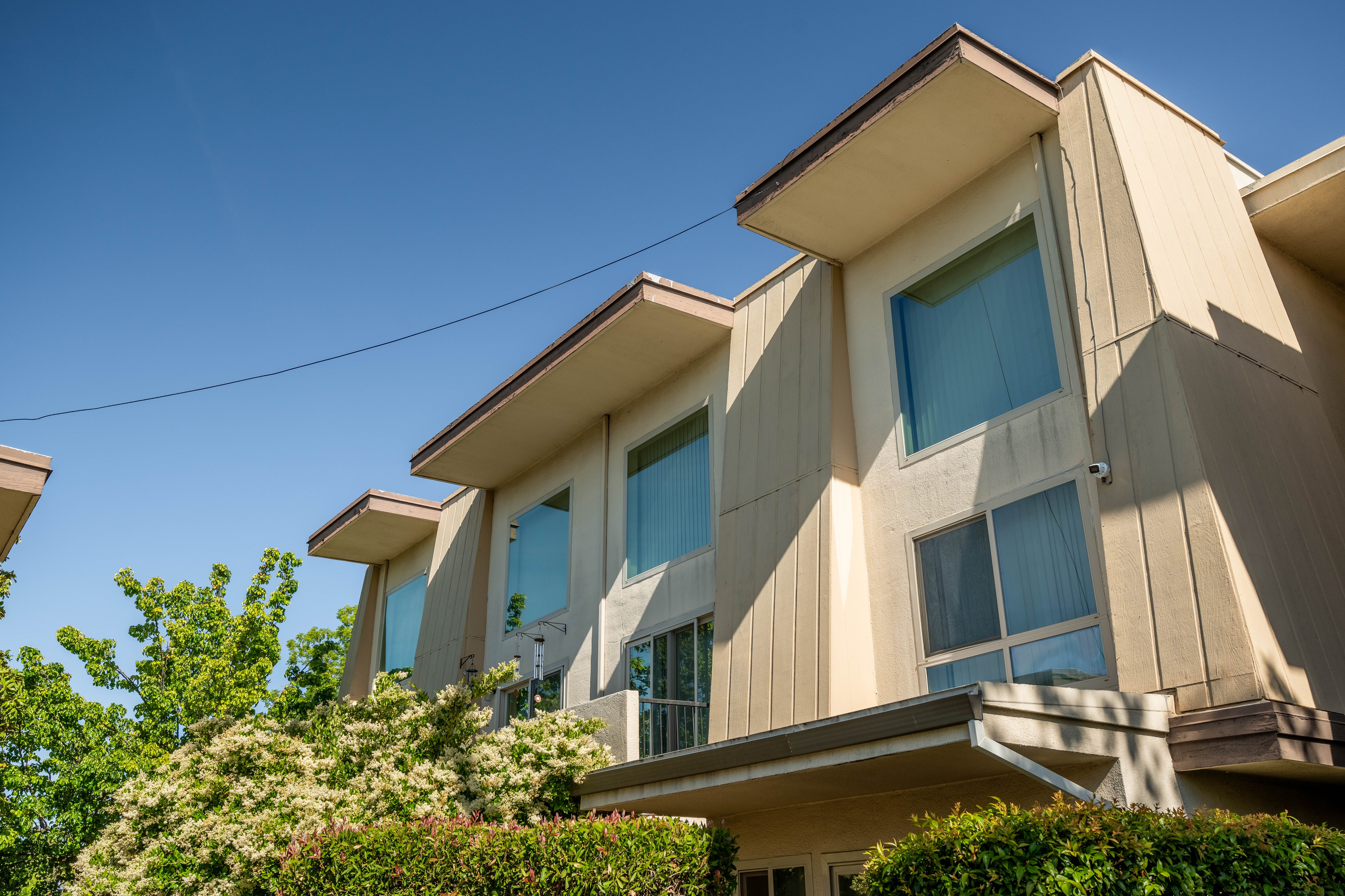 Exterior view of a modern building with large windows, surrounded by greenery under a clear blue sky.