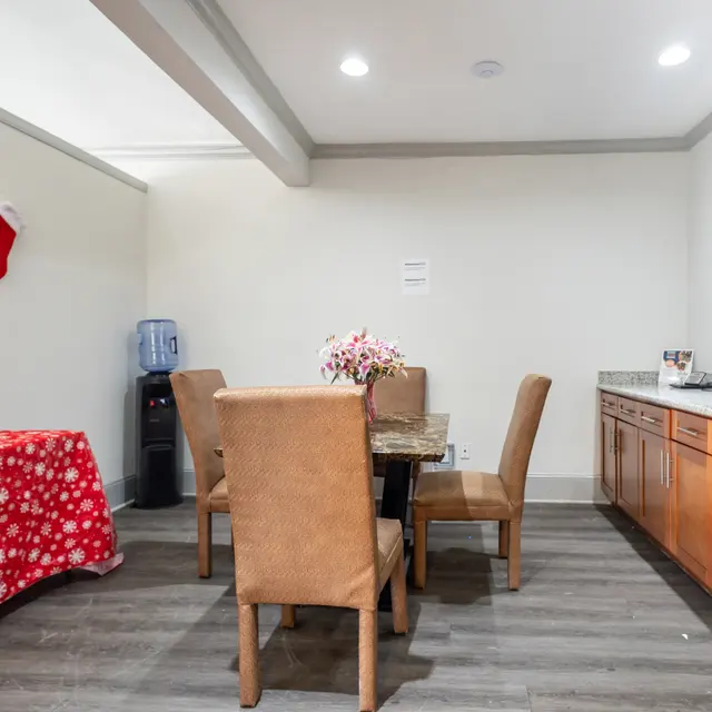 A cozy dining area decorated for Christmas with a red tablecloth featuring snowflakes, a water dispenser, a flower vase, and a kitchen counter with a coffee machine and wine fridge.