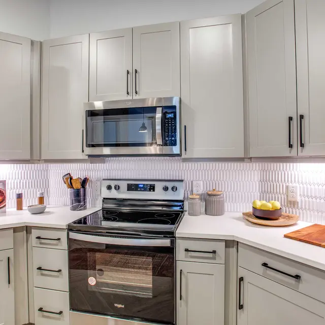 A modern kitchen featuring curved cabinetry, stainless steel appliances, and a white glossy backsplash. The kitchen has an island with wooden cutting boards and bowls, complemented by soft lighting.