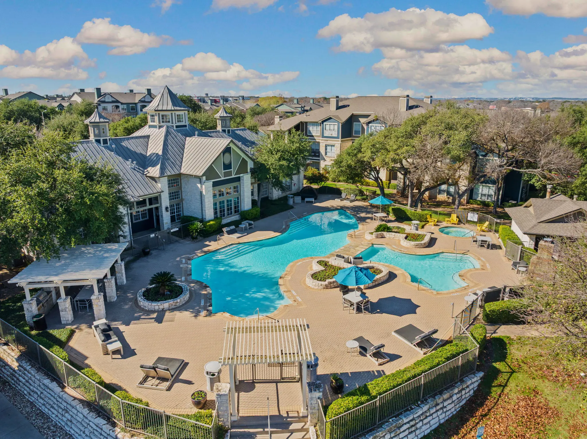 Aerial view of a luxurious apartment complex featuring a large swimming pool surrounded by landscaped greenery and lounging areas.