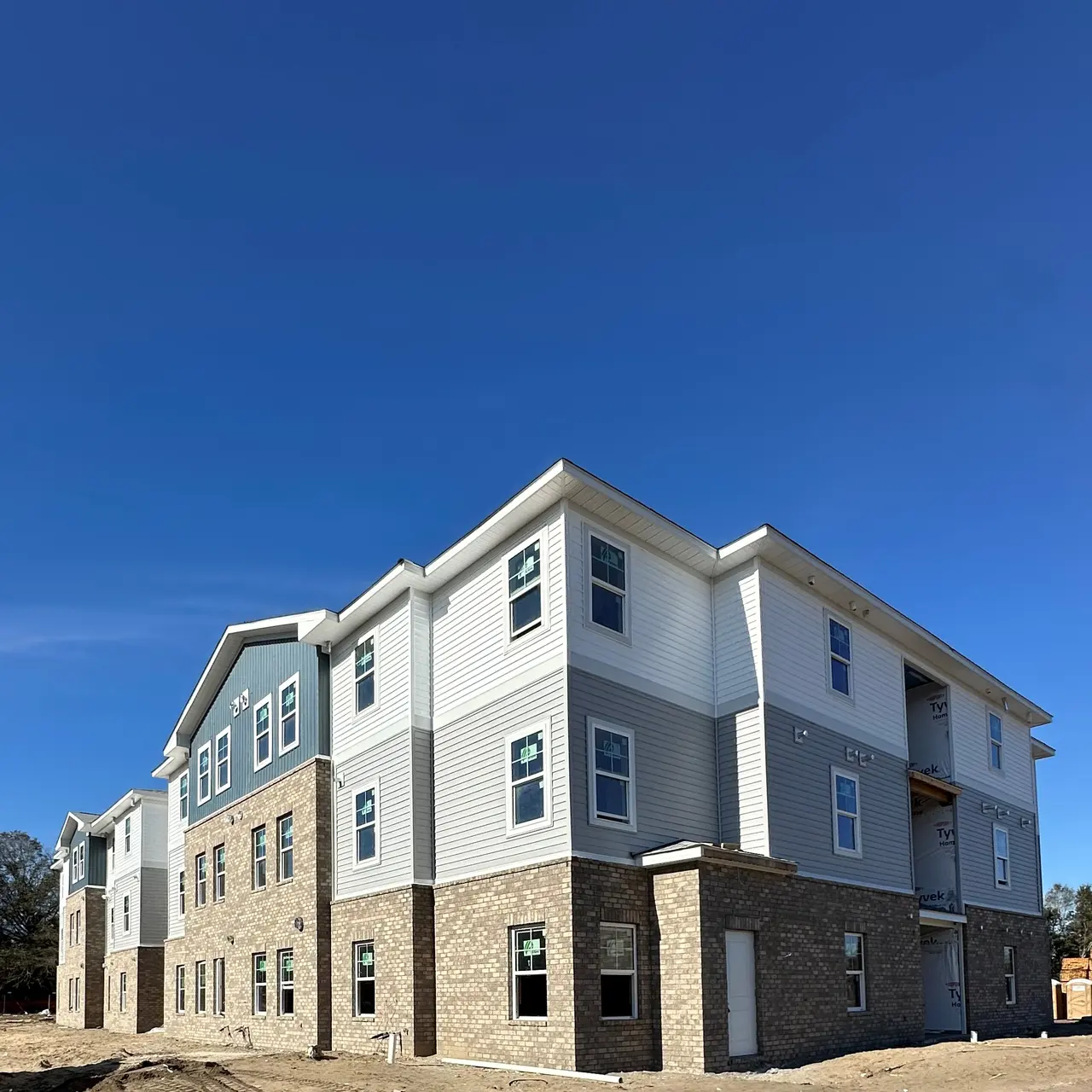 A newly constructed apartment building featuring a combination of gray and tan siding with multiple windows.