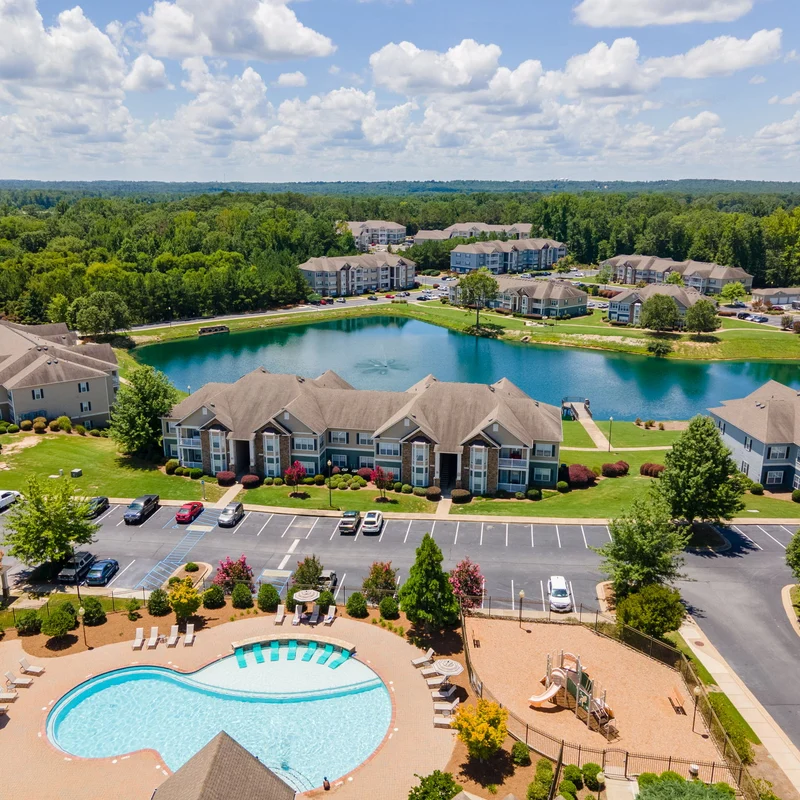Aerial View of Residential Community Aerial view of a residential community featuring a swimming pool, a pond, and several apartment buildings.