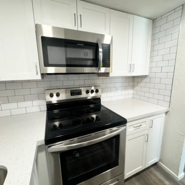 A modern kitchen featuring white cabinets, stainless steel appliances, and a clean, tiled backsplash. The focus is on the stove and microwave, with a sleek countertop.