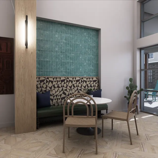 A modern interior space featuring a round table surrounded by four wooden chairs. One wall has a decorative wood panel, while another features textured teal tiles. Large windows let in natural light, revealing a view of outdoor seating.