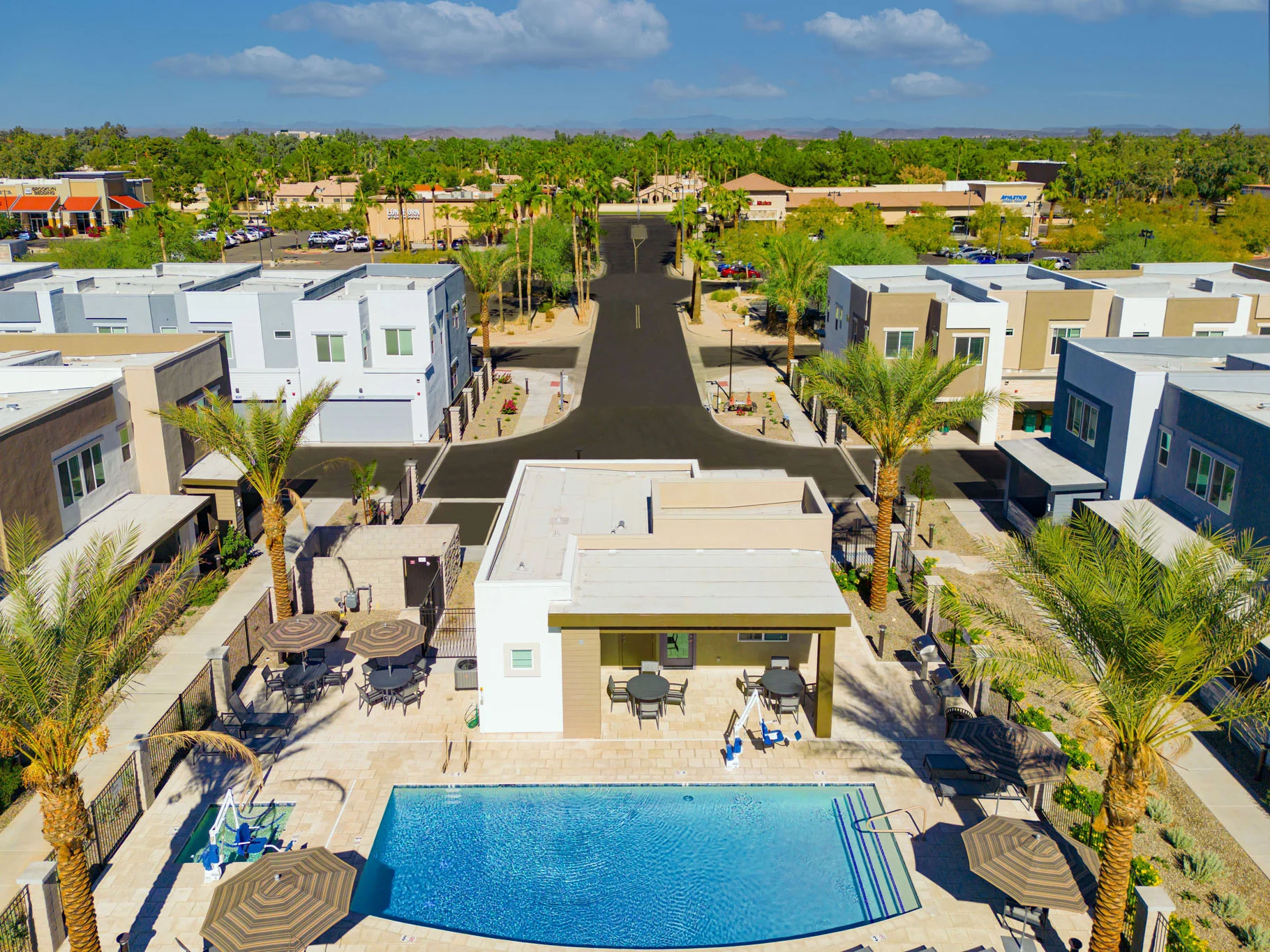 Modern Housing Development with Pool View Aerial view of a modern housing development featuring a swimming pool surrounded by palm trees and residential buildings.