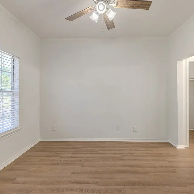 An empty room with wooden flooring and a ceiling fan, featuring a window with blinds on the left side and an open door leading to a closet on the right.