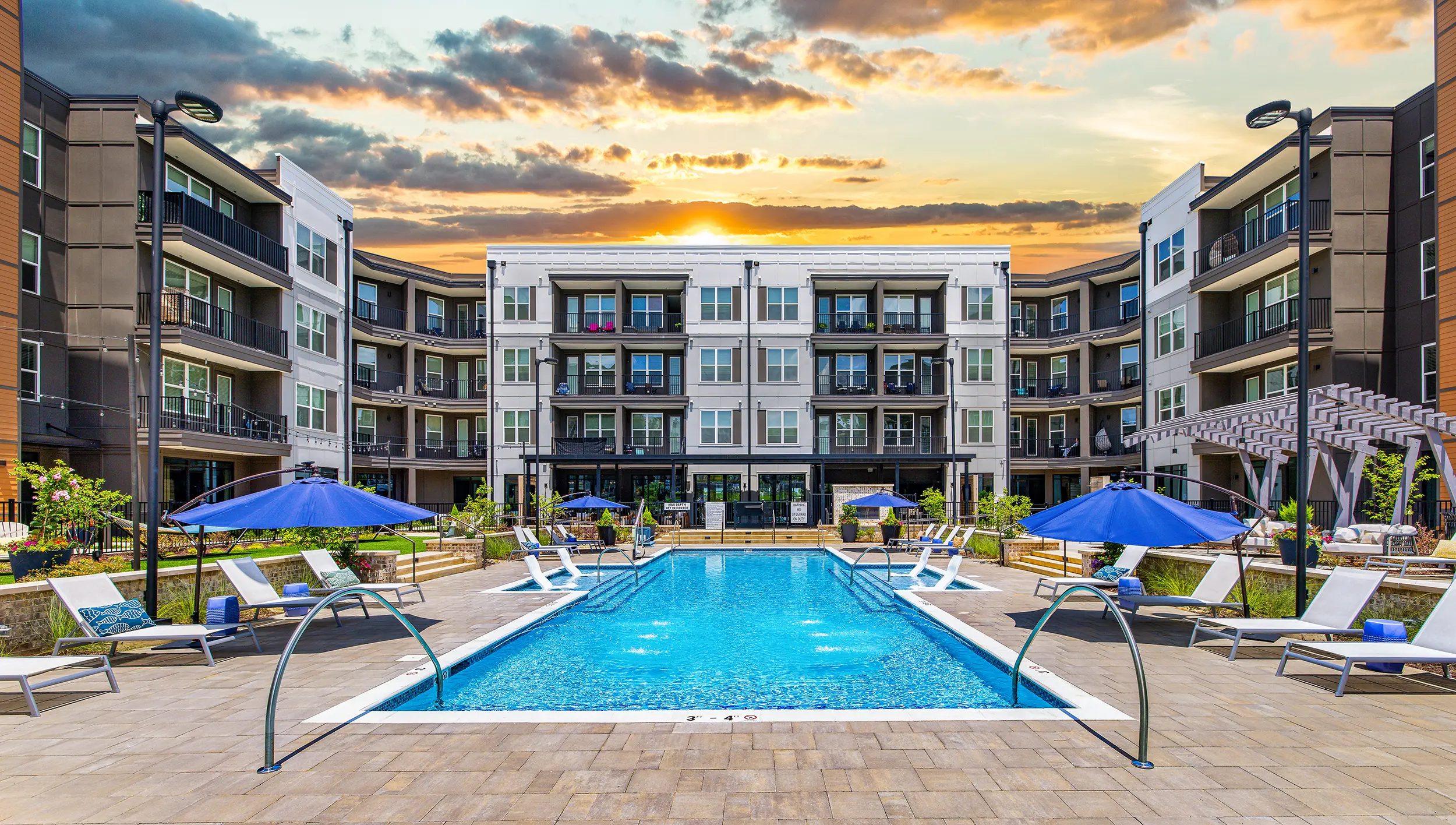 Modern Apartment Pool Area at Sunset Outdoor swimming pool area of a modern apartment complex during sunset, featuring lounge chairs and umbrellas.