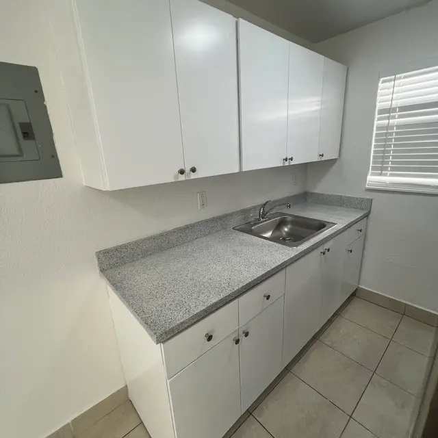 Modern kitchen with white cabinets, granite countertops, stainless steel sink, and tile flooring, featuring a window with blinds.