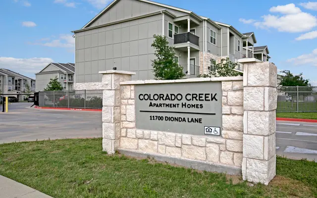 Sign for Colorado Creek Apartment Homes at 11700 Dionda Lane with modern apartment buildings in the background.