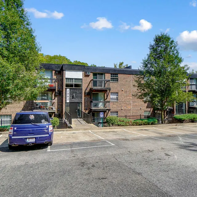 Exterior view of a brick apartment building with trees nearby and parked cars in the foreground.