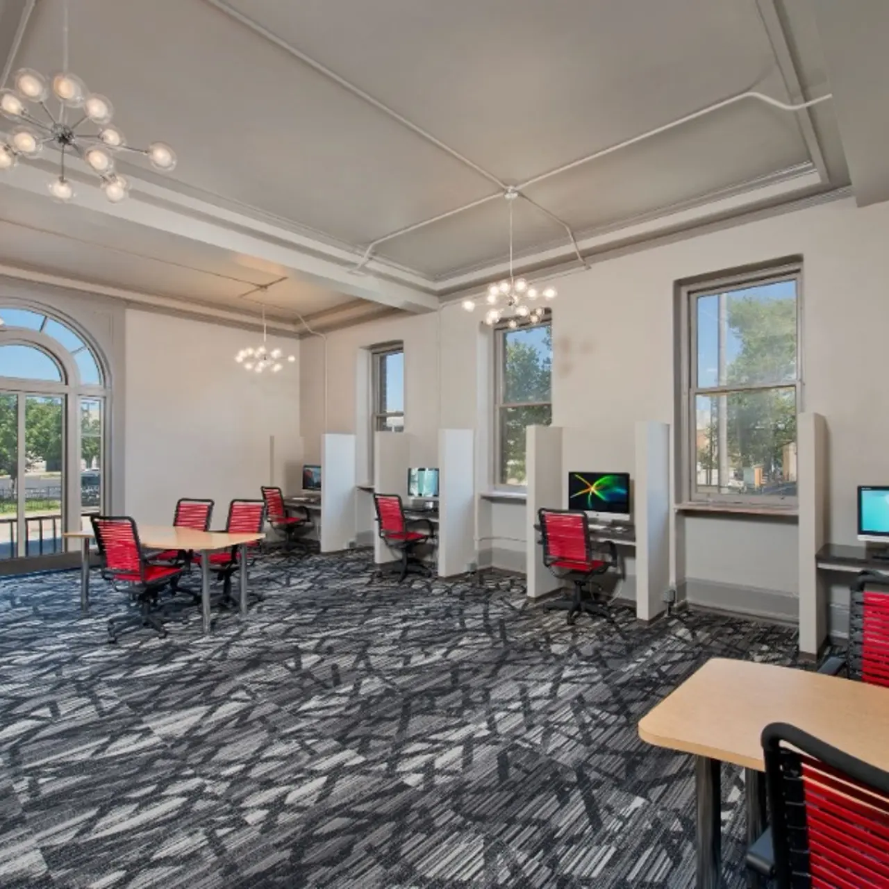 A spacious modern office interior with desks and computers, featuring a stylish carpet, large windows, and unique light fixtures.