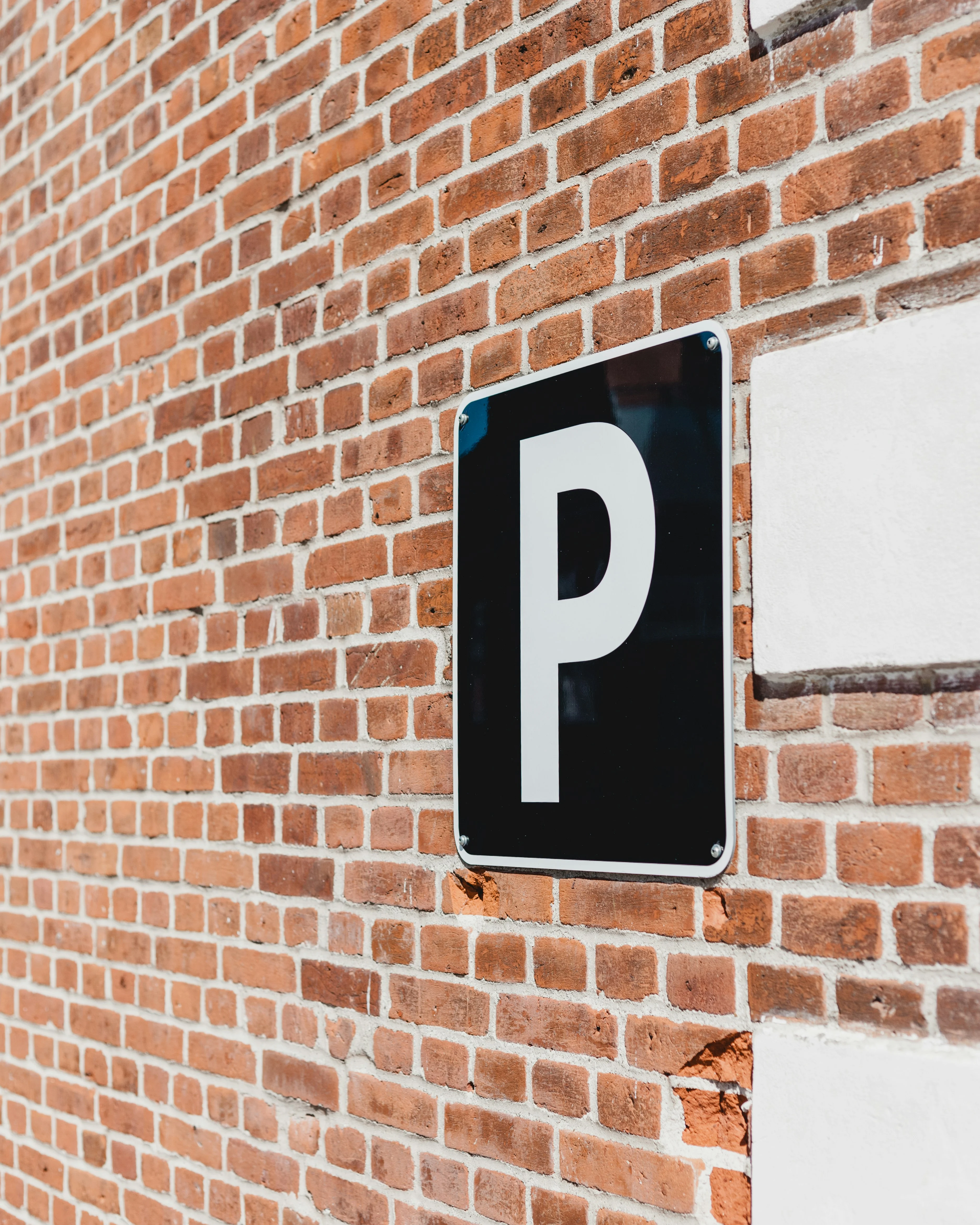 A black parking sign with a large white letter 'P' is mounted on a textured brick wall.