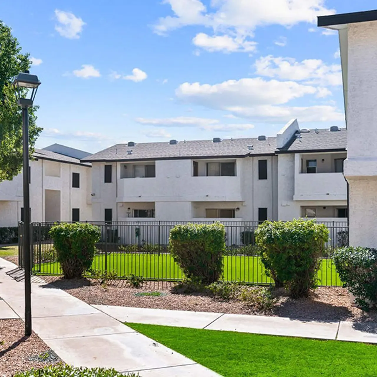 View of a modern apartment complex surrounded by landscaped areas and a fence.