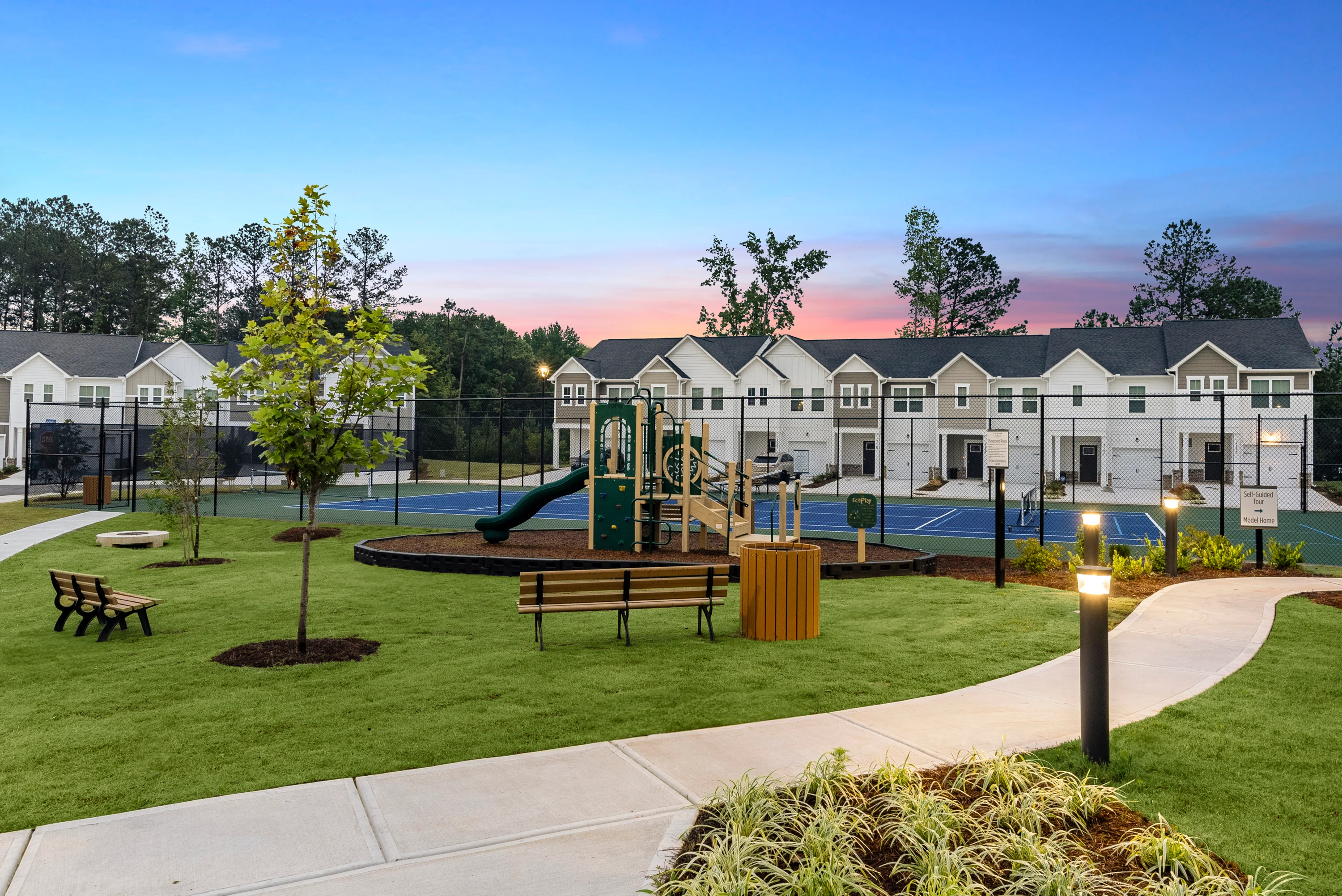Community Playground and Tennis Courts at Twilight A landscaped community area featuring a playground, tennis courts, and residential buildings in the background during twilight.