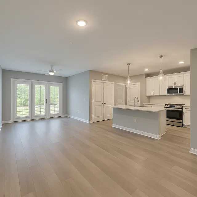 Modern Kitchen and Living Space A spacious room featuring an open layout with a modern kitchen and living area. The kitchen includes white cabinetry, and a central island with bar seating. Large double doors lead to an outdoor area, with natural light streaming in. Light wooden flooring complements the neutral color scheme.