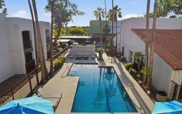 A sunny outdoor pool area surrounded by palm trees and buildings with white walls and terracotta roofs.
