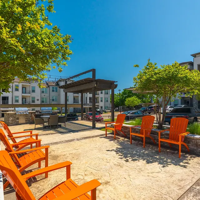 A sunny outdoor lounge area with orange chairs, surrounded by greenery and an apartment complex in the background.