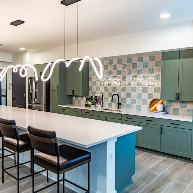 A modern kitchen featuring a long island with bar stools, vibrant green cabinetry, and a unique tile backsplash.