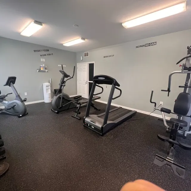 A well-equipped home gym featuring various exercise machines, free weights, and a TV on the wall.