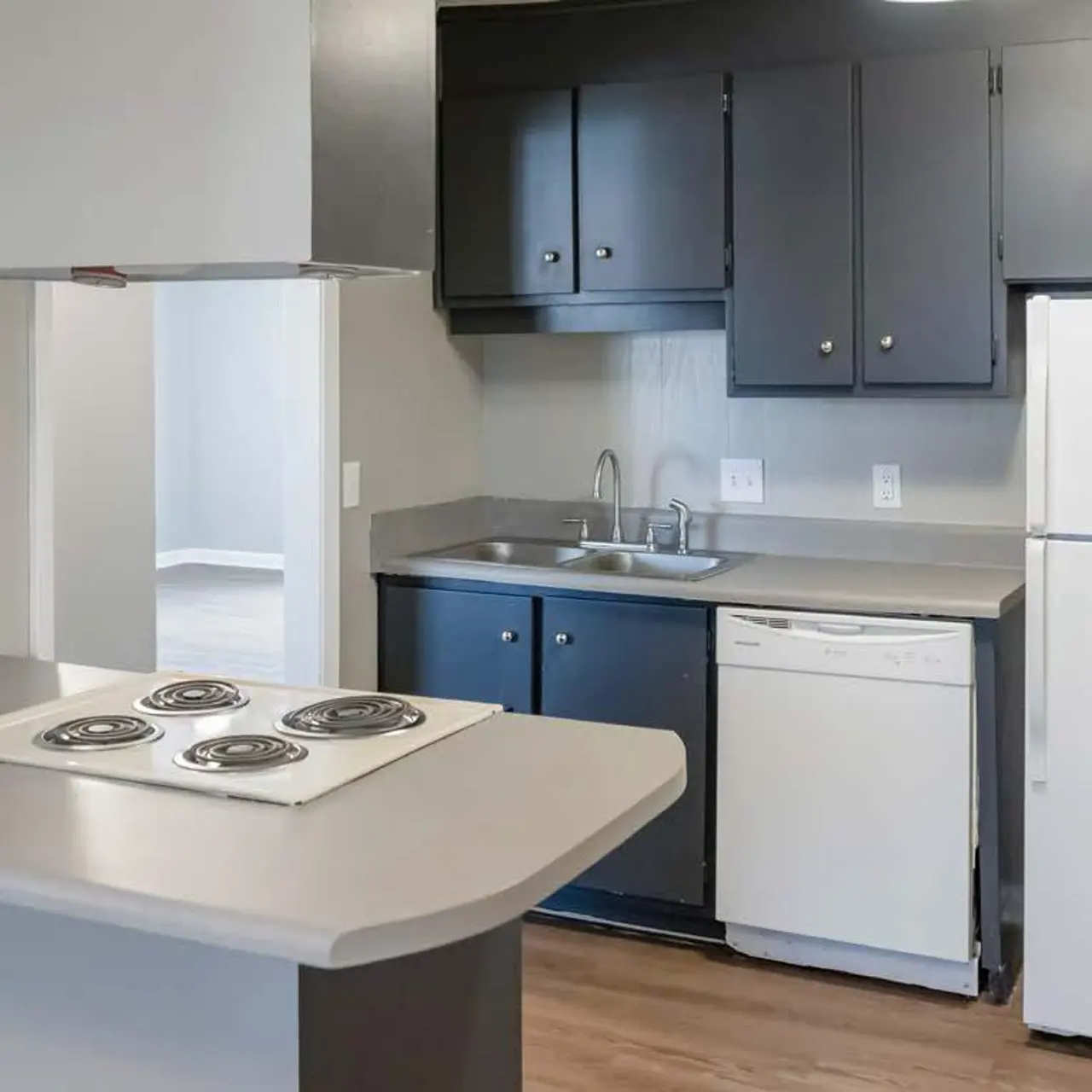 Haltere at Reserve - A modern kitchen with gray cabinetry, a white refrigerator, and a dishwasher. The countertop features a built-in stovetop with four burners.