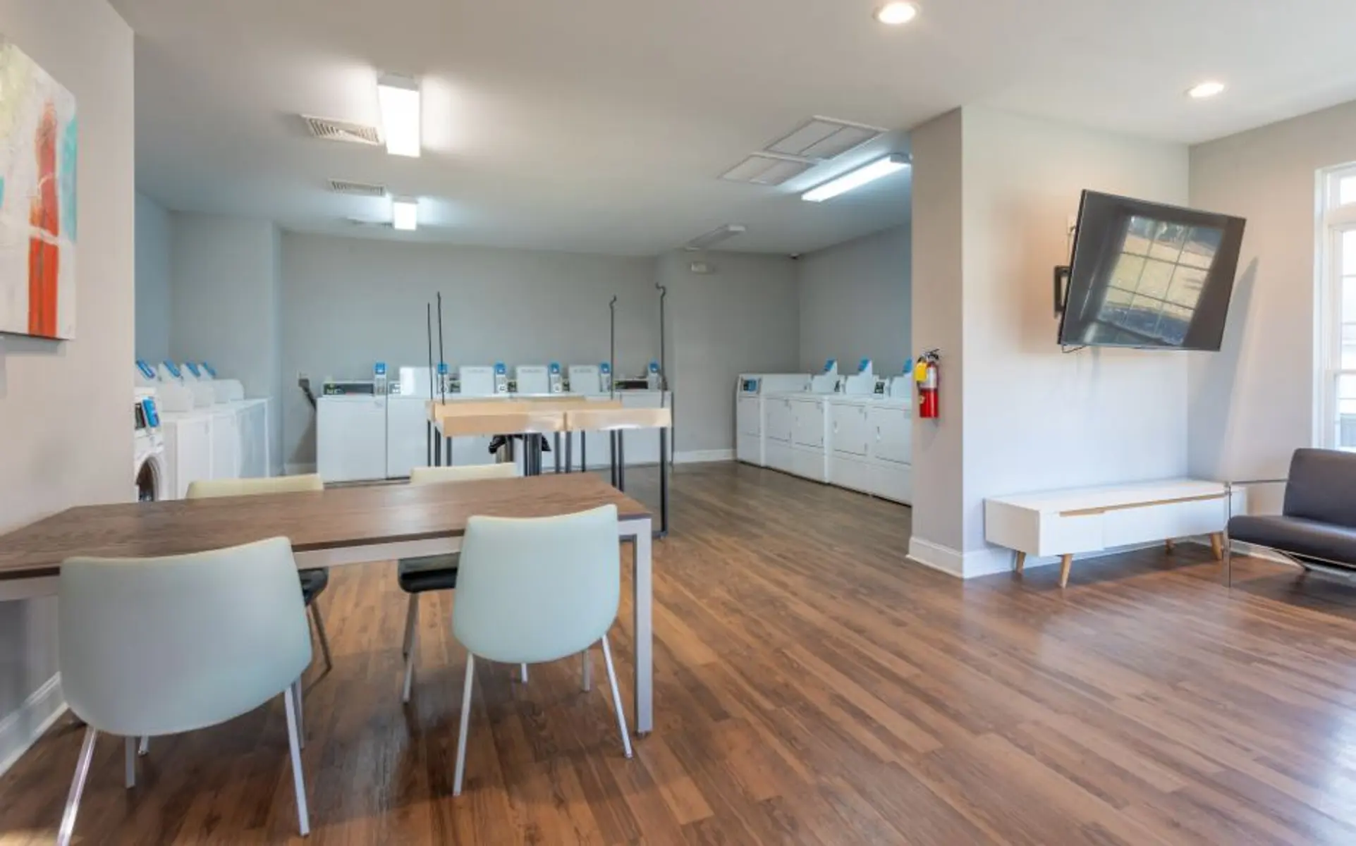 An interior view of a modern laundry room featuring tables and several washing machines in white cabinets.