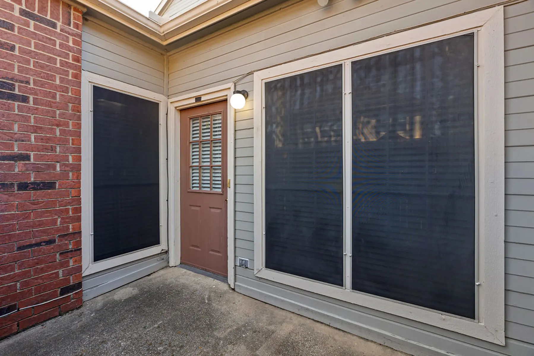 Entryway with Brick Accent and Screened Windows A covered entryway with a brown door and large windows covered with dark screens. The wall to the left is made of red brick, and the exterior is in neutral colors.