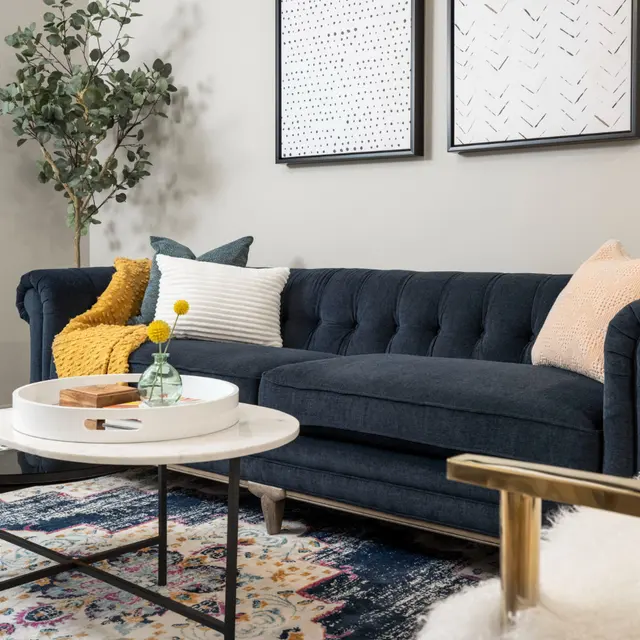 A stylish living room features a navy sofa, colorful cushions, a coffee table, and decorative art on the walls.