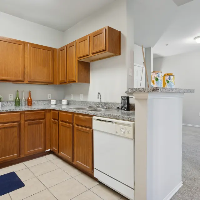 Modern kitchen featuring wooden cabinets, a white stove, and granite countertops, with a dishwasher and open layout to a living space.