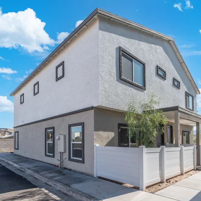 Contemporary Two-Story House Exterior A modern two-story house with a light gray exterior and black window frames. The house has a small porch and is surrounded by a white fence. The scene features a clear sky with fluffy clouds.
