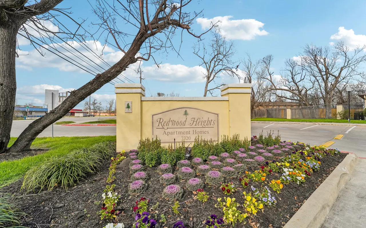 Entrance sign of Redwood Heights Apartments with colorful flowers and greenery in front.