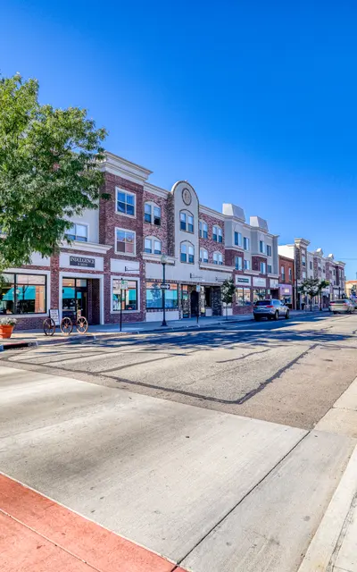 A wide view of a downtown street with modern buildings, lush trees, and clear blue skies.
