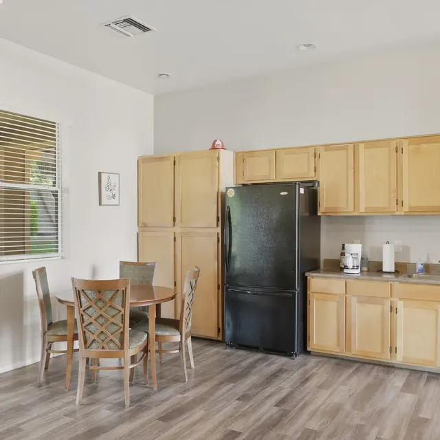 A modern kitchen featuring light wood cabinets, a black refrigerator, a dining table with four chairs, and a clean, spacious layout.