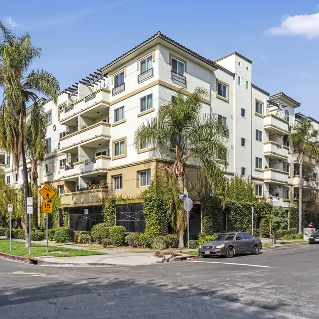 A modern multi-story apartment building with balconies and palm trees in the foreground.