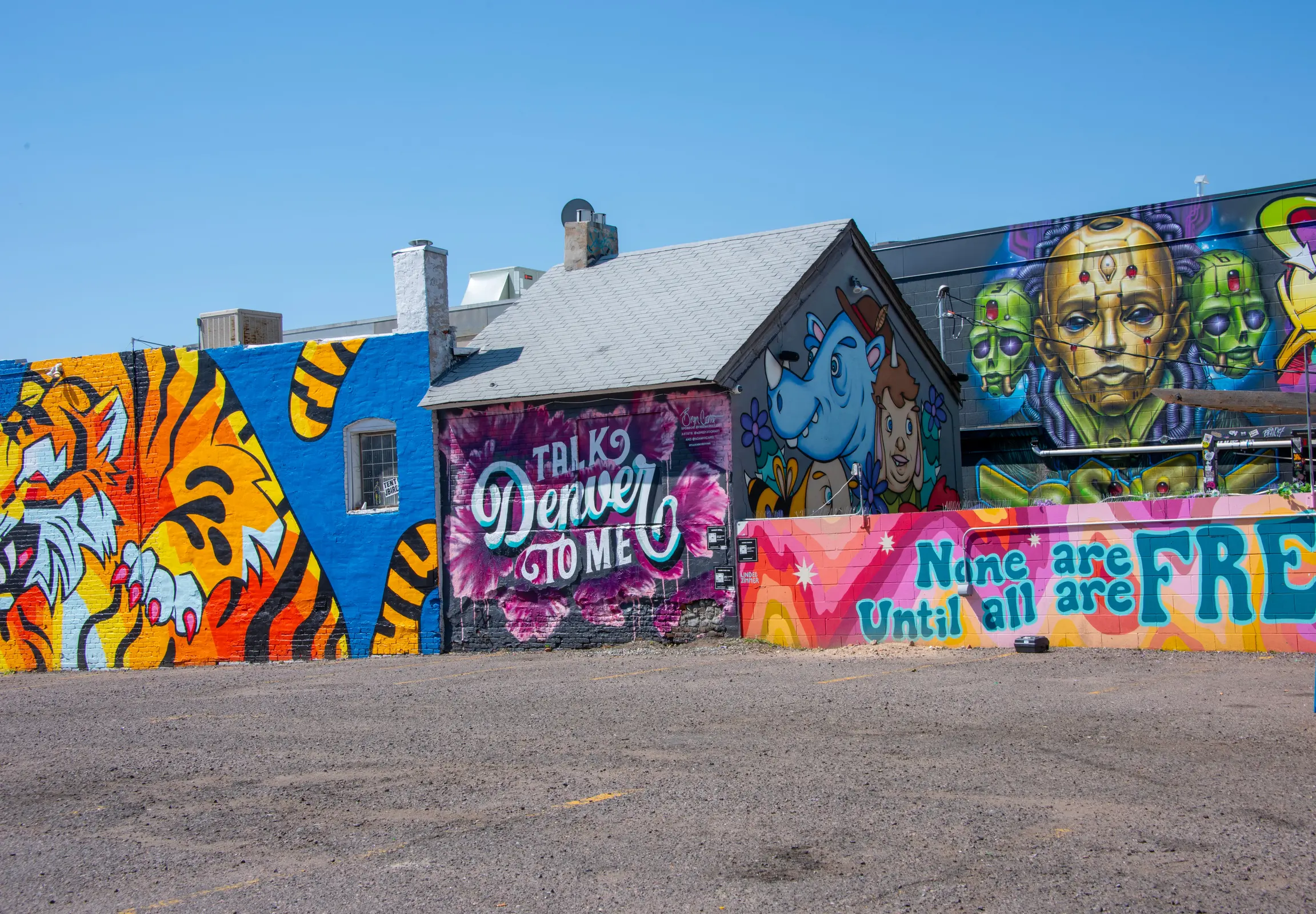 A vibrant street mural depicting various designs, including a tiger, a blue cartoonish character, and phrases related to Denver and freedom.