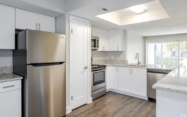 Modern Kitchen Design A modern kitchen with stainless steel appliances, including a refrigerator and stove, granite countertops, and white cabinetry. The space features a large window letting in natural light, and a wooden floor adds warmth to the design.