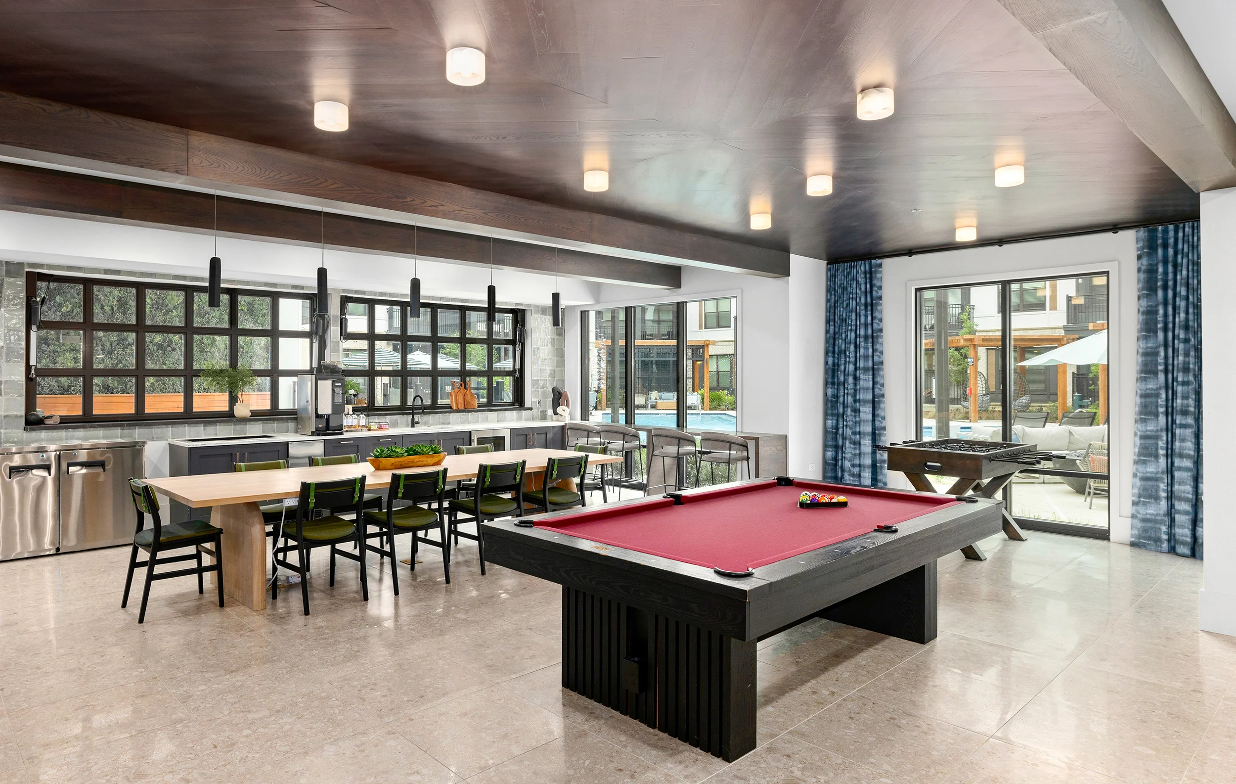 A contemporary indoor game room featuring a billiards table, a dining table, and large windows with a view of the outdoors.