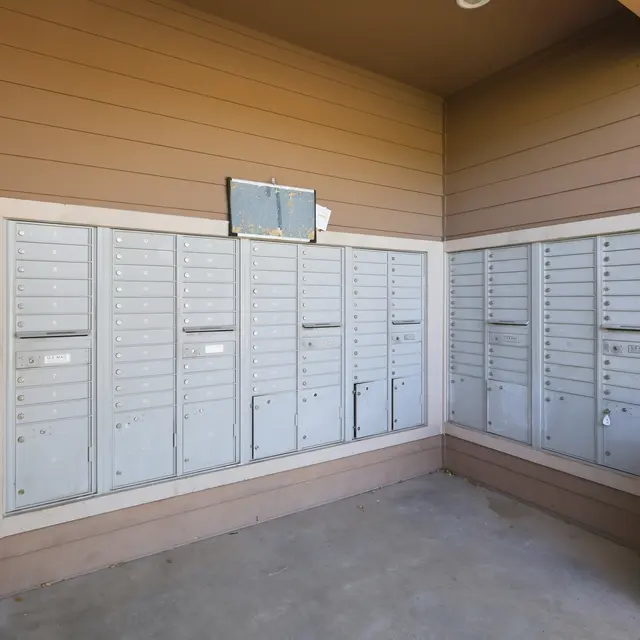 A row of gray mailboxes in a sheltered area with beige walls.