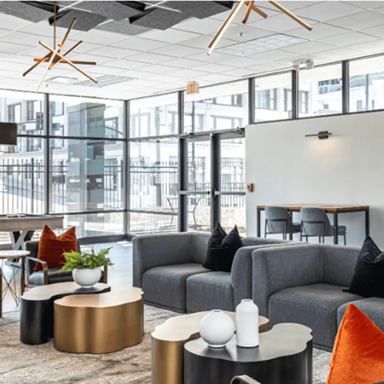 Contemporary Lounge Interior A modern lounge area featuring gray sofas, round tables, and decorative cushions in orange and black. Large windows allow natural light to fill the space, complemented by stylish light fixtures.