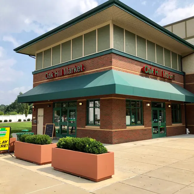 Oak Hill Market Entrance A photo of the Oak Hill Market building, featuring a green awning and brick exterior. The entrance has several glass doors and there are potted plants in front. A sign indicates a game or activity with the text 'PLAY HERE!'
