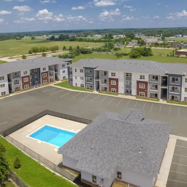 Aerial view of a modern apartment complex featuring multiple buildings, a parking area, and a swimming pool.
