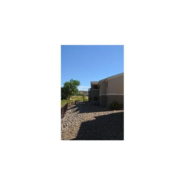 A sunny day view of a landscaped area beside an apartment building, featuring a gravel path and green trees.