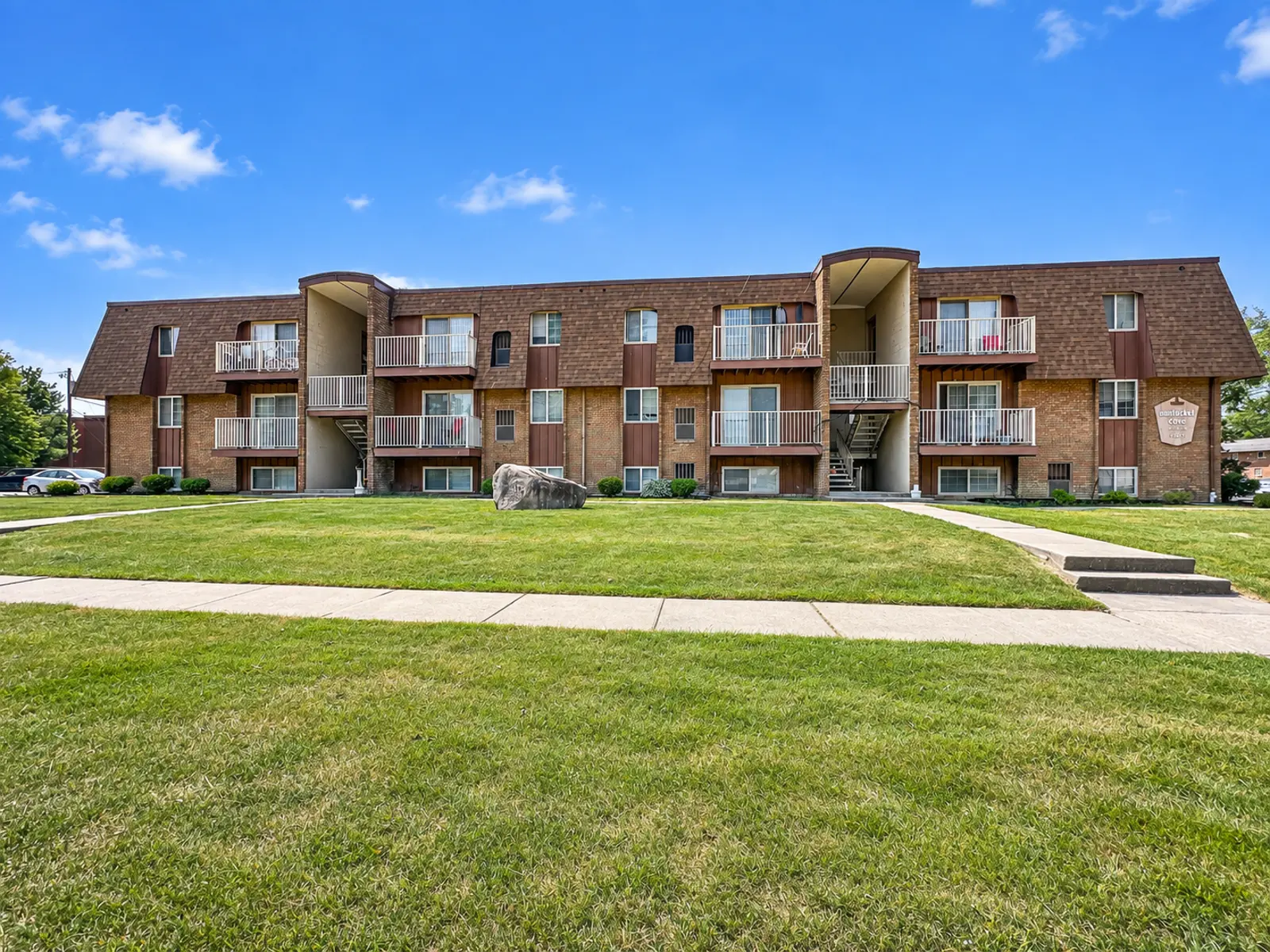 Exterior view of a multi-unit apartment building with balconies and green lawn in front.