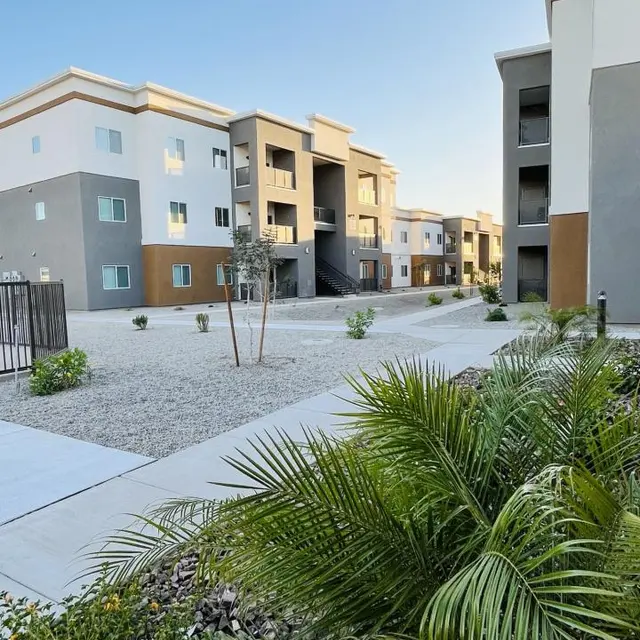 View of a modern apartment complex with several buildings surrounded by a gravel area and greenery.