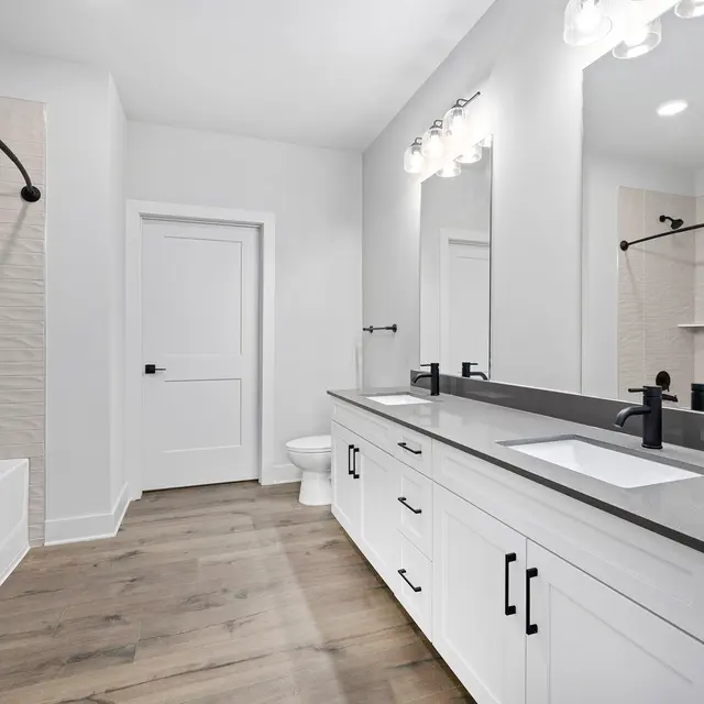Modern Bathroom Design A modern bathroom featuring a white bathtub, black fixtures, a dual sink vanity with a grey countertop, and large mirrors. The walls are mostly white with a stylish textural element. The floor is made of light wood.