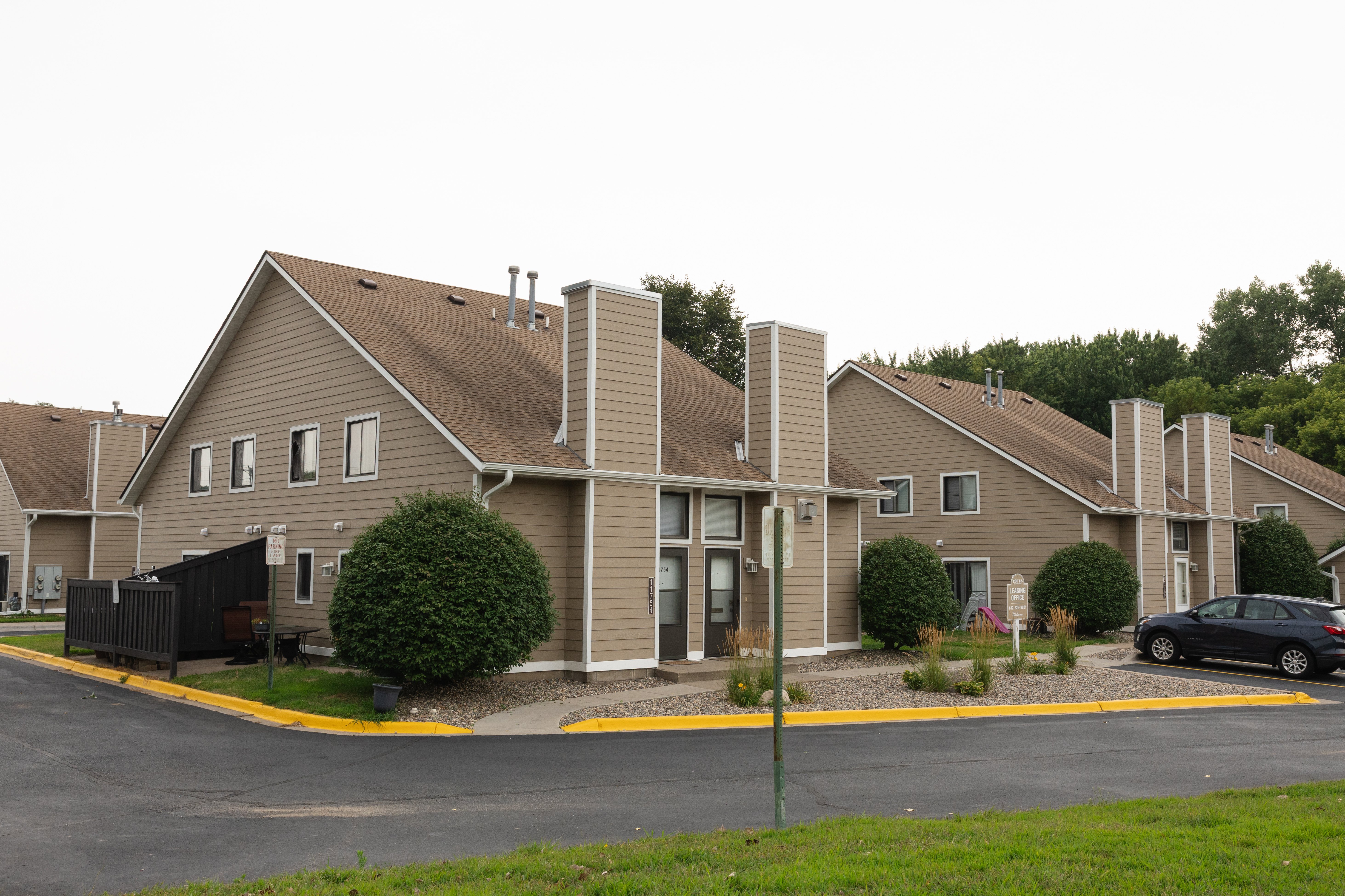 Residential Apartment Complex A view of several two-story apartment buildings in a residential complex featuring muted brown siding, landscape greenery, and a parking lot.