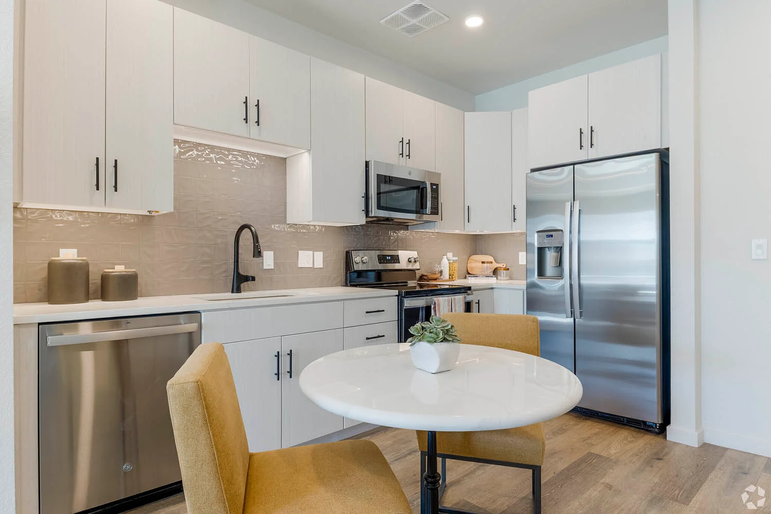 Contemporary Kitchen and Dining Space A modern kitchen with light-colored cabinetry, stainless steel appliances, and a small dining area featuring a round table and two chairs.