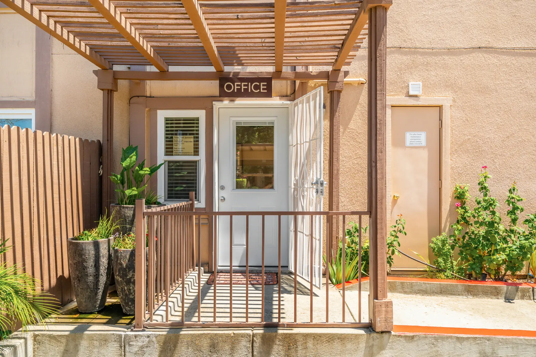 Entrance to an office with a covered porch, door labeled 'OFFICE', surrounded by greenery.