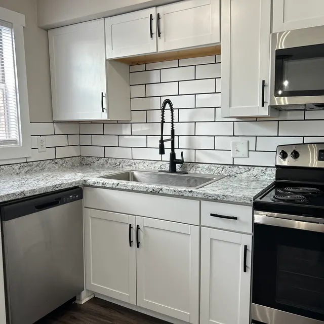A modern kitchen featuring white cabinetry, a stainless steel sink, and a granite countertop. The backsplash consists of white subway tiles. There are stainless steel appliances including a range and microwave, along with a dishwasher.