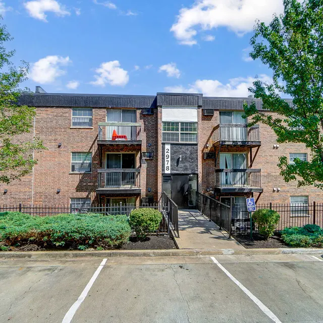 Front view of a multi-story apartment building with balconies and trees surrounding it.