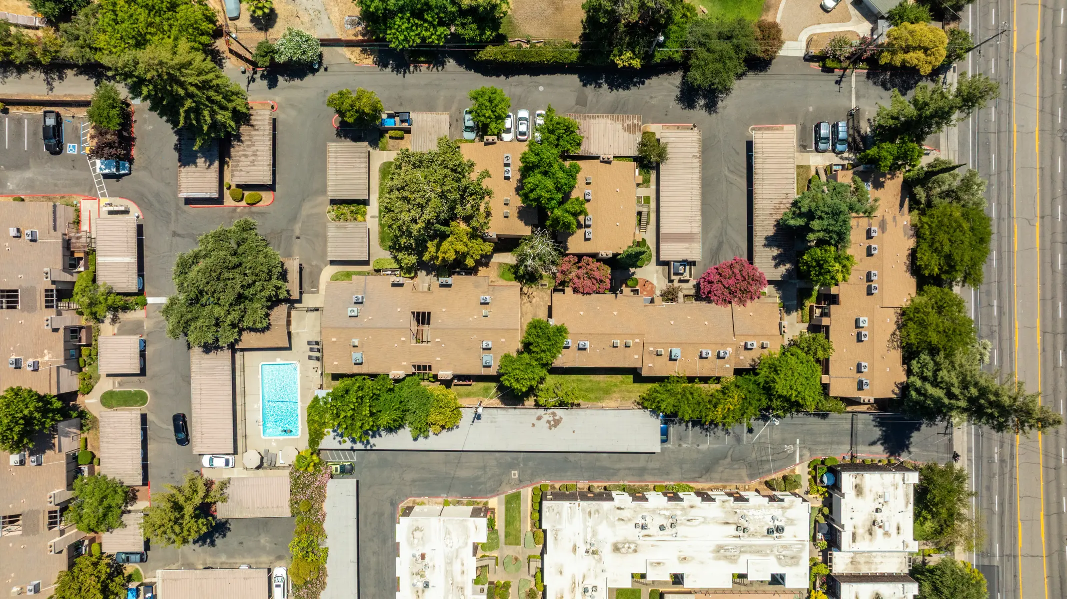 Aerial view of a residential area featuring several apartment buildings, a swimming pool, and surrounding greenery.